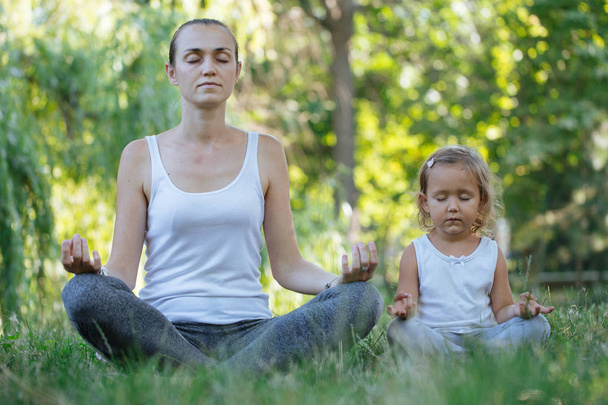 Young mother and cute little daughter meditating in lotus pose together - Photo, image