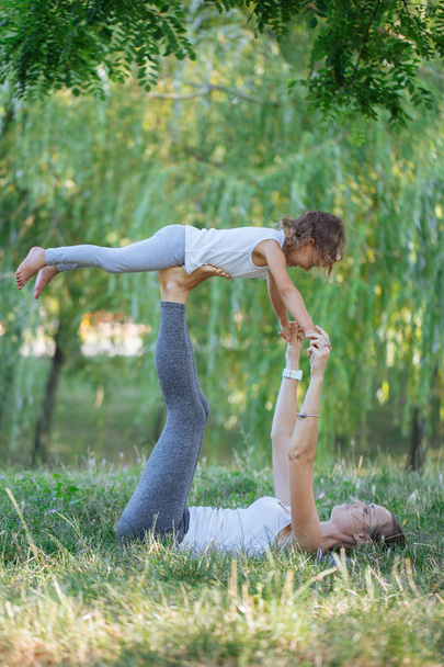 Mother and daughter doing yoga exercises on grass in the park at the day time. - Foto, Imagen
