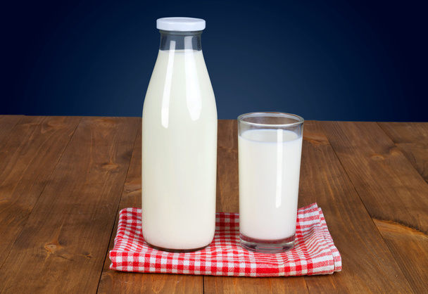 Täysi pullo tuoretta maitoa ja yksi lasi on puinen pöytä sinisellä pohjalla
 - Valokuva, kuva