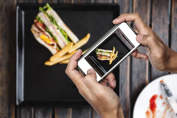 Taking food photo, food photography by smart phone, club sandwich with french fries on wooden table - Photo, Image