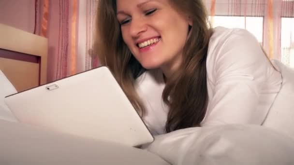 Young happy woman using tablet computer lying in white bed - Video