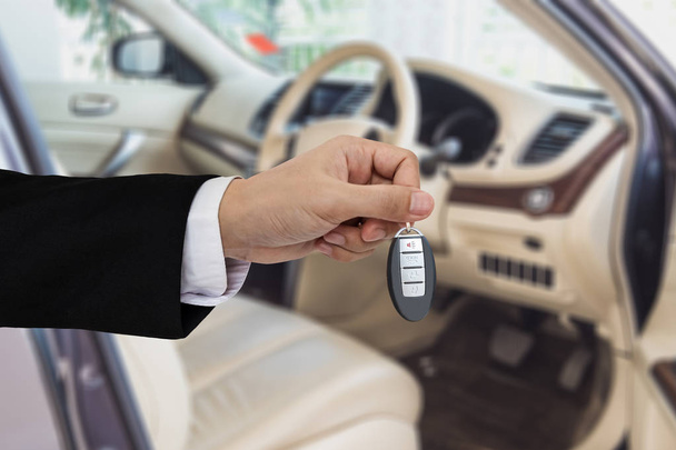 Χέρι που κρατά το κλειδί του αυτοκινήτου απομακρυσμένη με, σύγχρονο αυτοκίνητο φόντο - Φωτογραφία, εικόνα
