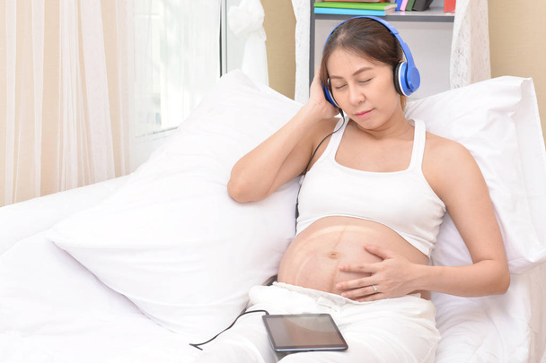 Pregnant women are listening to music through headphones. - Φωτογραφία, εικόνα