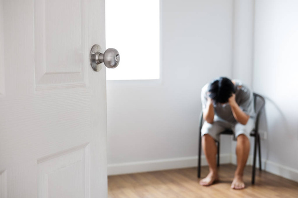 Puerta abierta con chico deprimido sentado en la esquina de la habitación vacía
 - Foto, Imagen