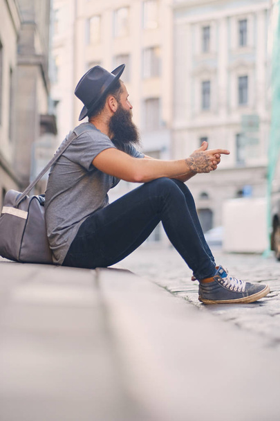 hipster barbudo se sienta en un escalón en una calle
 - Foto, Imagen