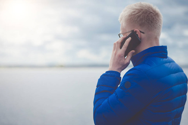 Blonde man using mobile phone at lake - Foto, Bild