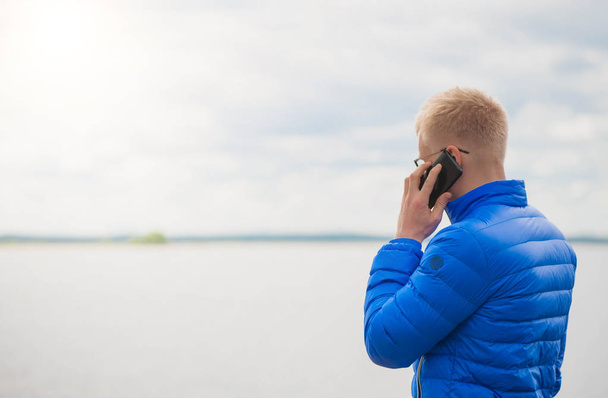 Blonde man using mobile phone at lake - 写真・画像