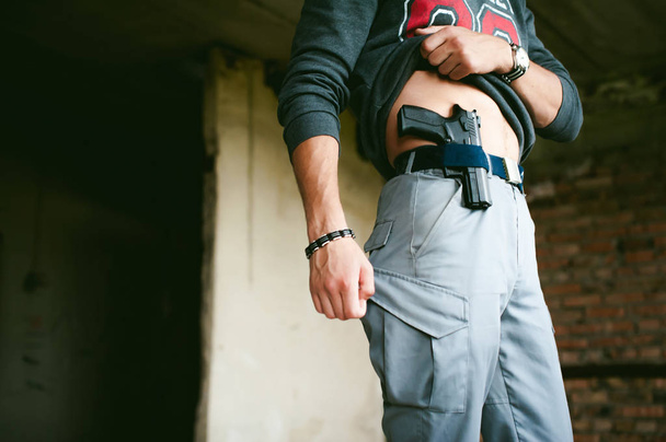 joven atlético sosteniendo un arma detrás de su cinturón
. - Foto, Imagen