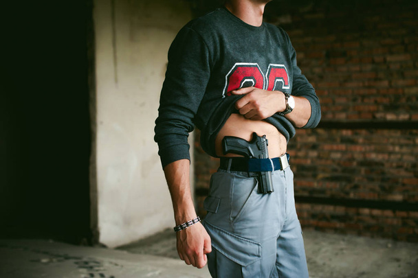 young athletic man holding a gun behind his belt. - Φωτογραφία, εικόνα