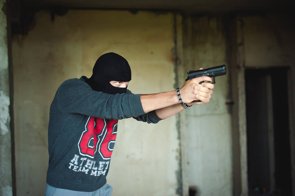 Athletic man in a balaclava, holds a pistol in his hand, is threatened with shooting, aiming - Foto, afbeelding
