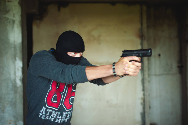 Athletic man in a balaclava, ski mask on his head, holds a gun in his hand - Foto, afbeelding
