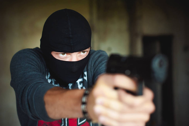 Athletic man in a balaclava, holds a pistol in his hand, is threatened with shooting, aiming - Photo, image