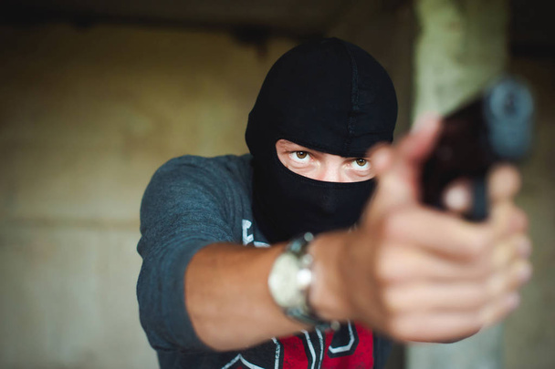 Athletic man in a balaclava, holds a pistol in his hand, is threatened with shooting, aiming - Foto, Imagem