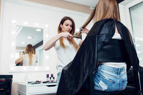 Peluquería femenina joven sosteniendo una hebra peinando pelo largo de la muchacha en el salón de belleza
 - Foto, Imagen