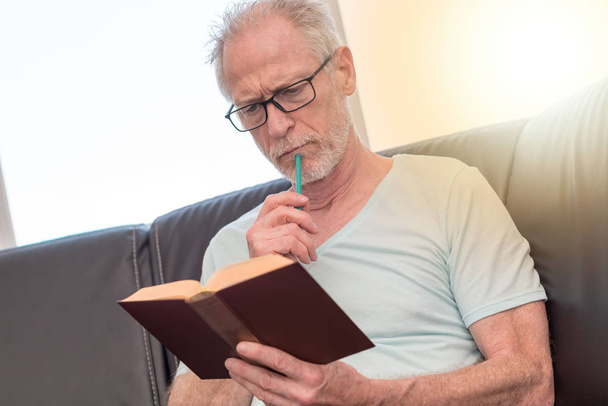 Portrait of thoughtful mature man reading a book, light effect - Fotó, kép