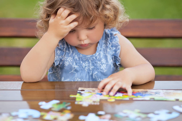 Difficult task. Tired child playing jigsaw with serious face.  - 写真・画像