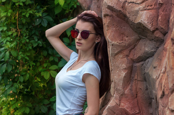 portrait of a beautiful lady in sunglasses which poses near a stone wall - Fotó, kép