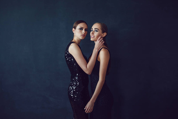 Two beautiful women in black night fashion dress posing on a black background. - Фото, изображение