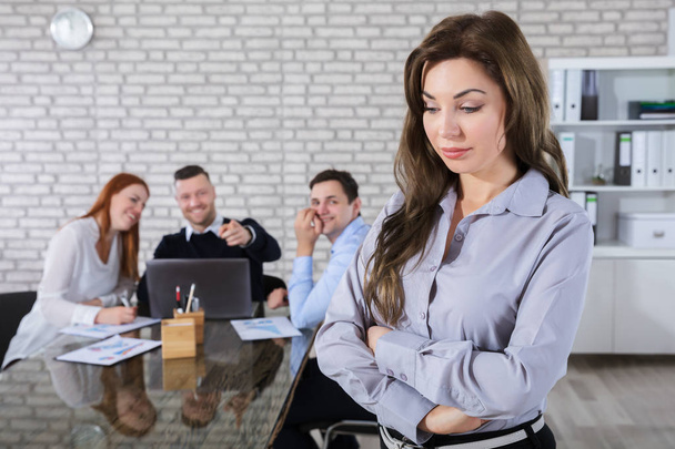 Portrait Of A Sad Businesswoman With Colleagues Laughing On Her In Background - Photo, Image