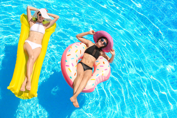 Beautiful young girls with inflatable donut and mattress in blue swimming pool - Foto, immagini