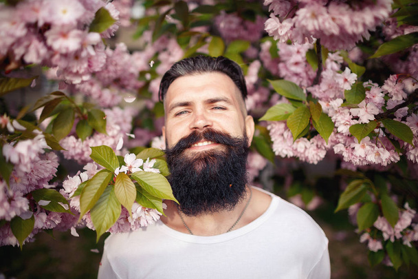 Un uomo barbuto allegro con bellissimi baffi, un elegante hairdress vicino alle foglie di sakura
 - Foto, immagini
