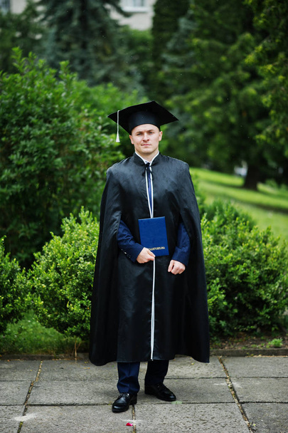 Portrait of an elegant young man in park dressed in graduation g - Photo, Image