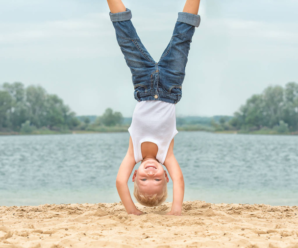 Little boy doing a handstand on the beach.Summer recreation and sports. - Фото, зображення