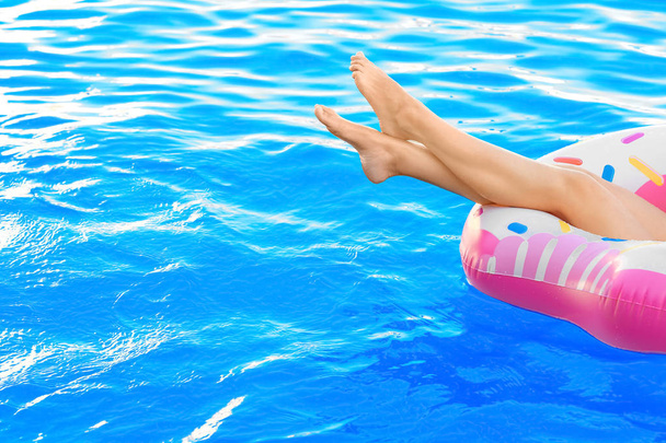 Young woman relaxing on inflatable donut in swimming pool - 写真・画像