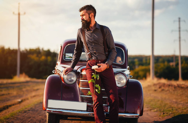 Elegante uomo barbuto con una rosa bianca in attesa per la sua amata vicino alla sua auto rossa
 - Foto, immagini