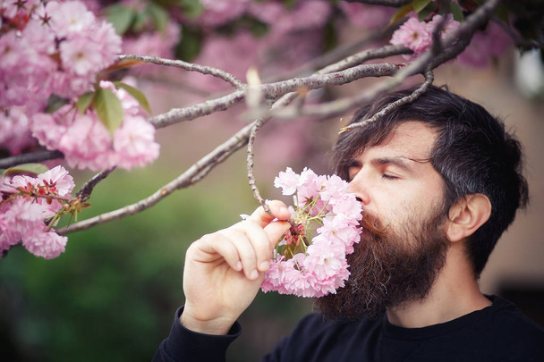 Egy brutális szakállas férfi egy stílusos frizurával áll mellette egy virágzó sakura - Fotó, kép