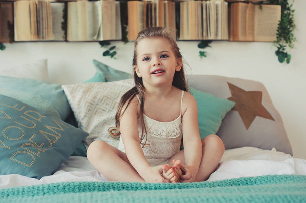 bonito menina criança feliz sentado na cama no pijama. Criança brincando em casa, captura de estilo de vida casual
. - Foto, Imagem
