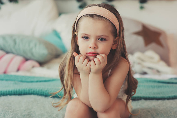 indoor portrait of sad 5 years old child girl sitting on bed in pajama - Zdjęcie, obraz
