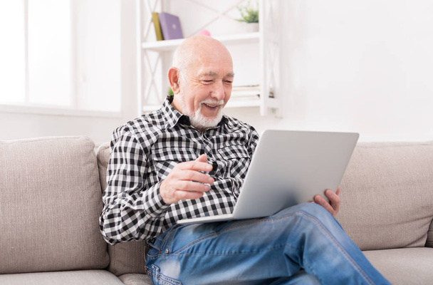 Smiling senior man reading news on laptop - Foto, Imagen