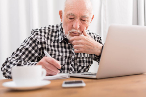 Mature man using laptop and writing in notepad - 写真・画像
