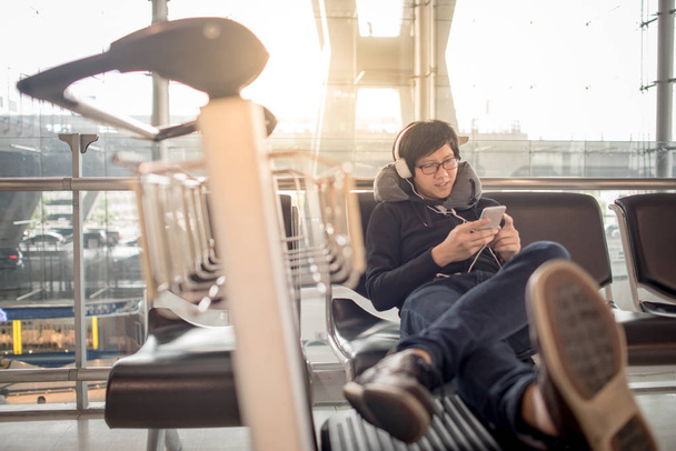 Asijský mladík poslechu hudby při čekání na letišti - Fotografie, Obrázek