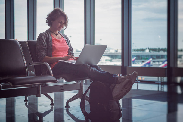 Young beautiful woman traveler sits at the airport with a laptop - Valokuva, kuva