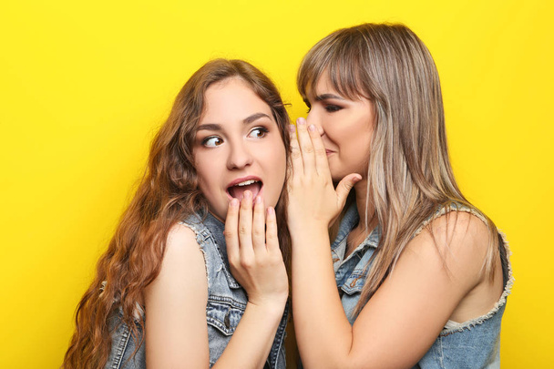 Two young woman whispering a secret on yellow background - Foto, immagini