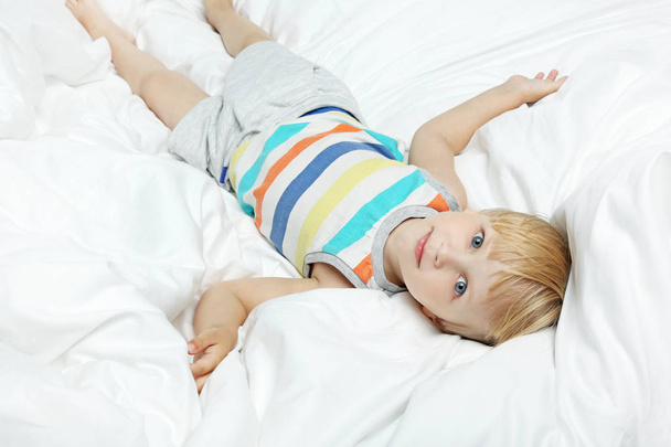 Little boy lying in white bed - Фото, изображение