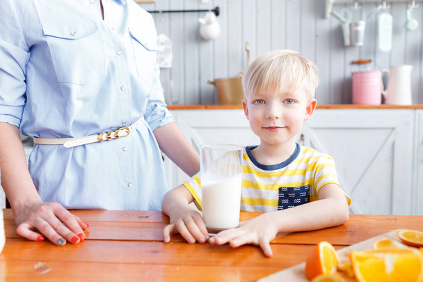 Mother and son are smiling while having a breakfast in kitchen. Mom is pouring milk into glass - Foto, imagen