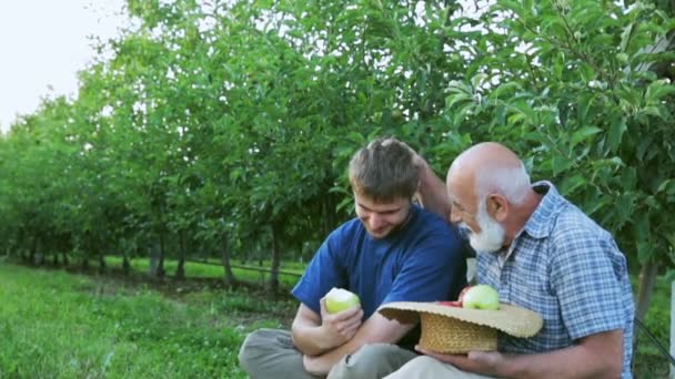 Happy grandfather with a grandson rest in an orchard. Grandfather brings her hair out of happiness - Footage, Video
