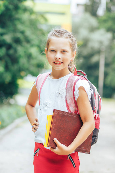 Schoolgirl with a backpack and a book in hands - Fotó, kép