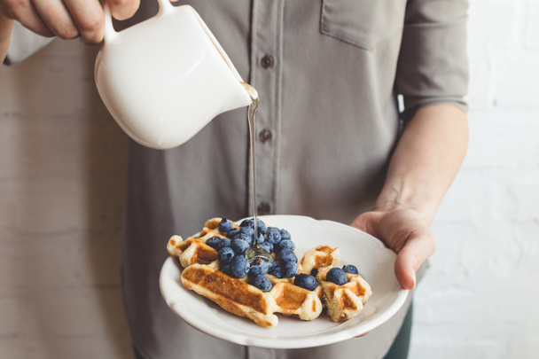 woman pouring syrup on tasty waffles - Foto, afbeelding