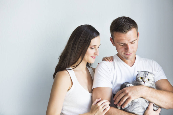 Young man with pregnant woman and cat indoors - Фото, изображение
