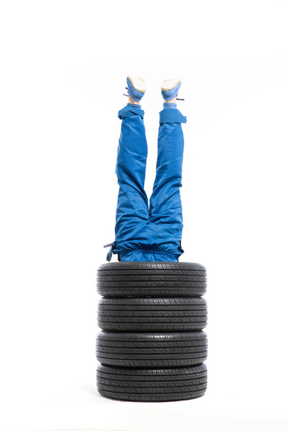 piernas de trabajador que sobresalen de la pila de neumáticos
 - Foto, Imagen