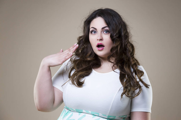 Surprised plus size fashion model, fat emotional woman on beige background, overweight female body - 写真・画像