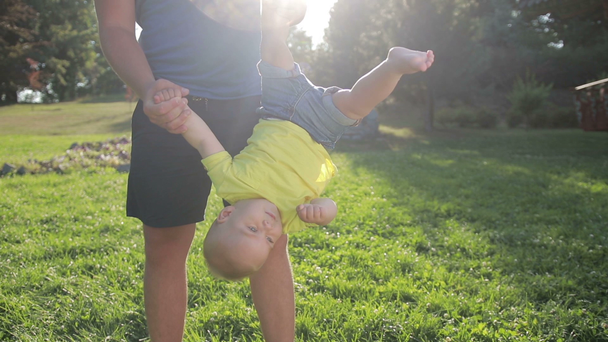 Ojciec kołysanie syn malucha nogami w parku - Materiał filmowy, wideo