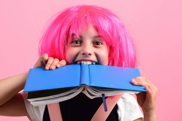 School girl bites big blue book isolated on pink background. - Foto, immagini