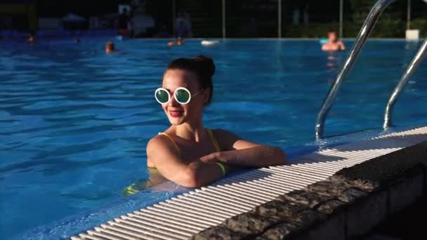 A beautiful woman in stylish glasses is in the pool, she enjoys a warm day - Πλάνα, βίντεο