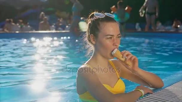 A cute and young woman with a good mood enjoys an ice cream in the pool - Materiał filmowy, wideo