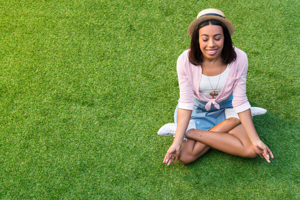 アフリカ系アメリカ人の女の子が芝生の上で瞑想 - 写真・画像